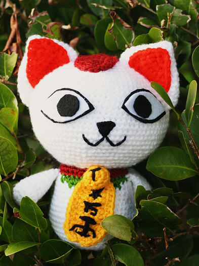 A lucky cat stands amongst leaves.