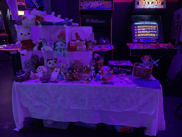 A six foot long table with grid cubes filled with handmade crochet stuffed animals from anime and video games. On top of the second layer of grid cubes is the light dragon from tears of the kingdom.