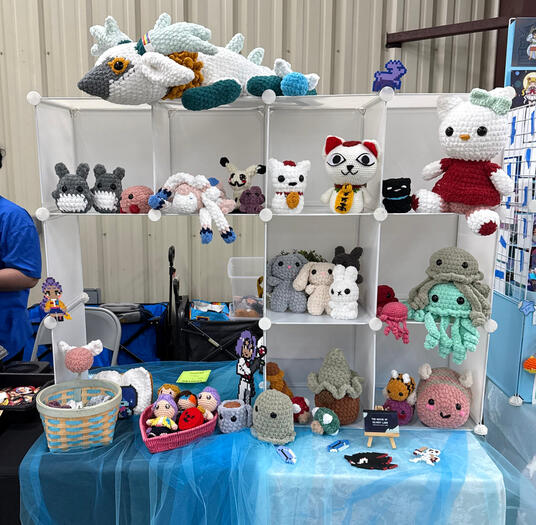 A four foot booth setup with eight grid cubes full of handmade crochet plushies from Pokemon, Studio ghibli, Sanrio, Legend of Zelda and more.